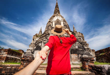 Tourist Woman in red shirt holding her husband by hand and going to ancient stupa in Ayutthaya Historical Park, Thailandの写真素材