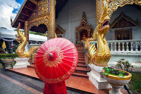 Woman tourist with red traditional Thai umbrella near Golden temple Wat Phra Singh with Big Dragon...