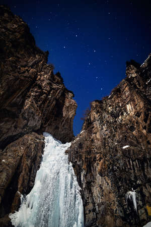 Frozen waterfall in the winter night mountain at starry sky with Big Dipper constellation