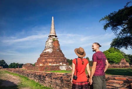 Young Couple in red clothes with photo camera looking at ancient ruined Wat Mahathat in Ayutthaya, Thailandの写真素材