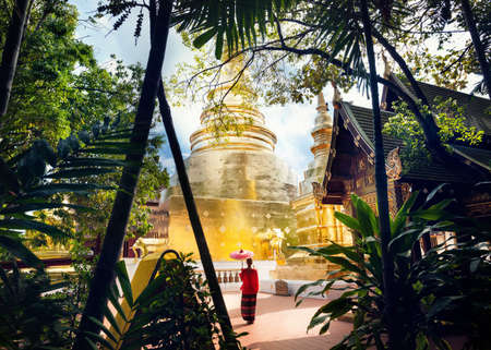 Woman tourist with red traditional Thai umbrella near Golden temple Wat Phra Singh in Chiang Mai, Thailandの写真素材