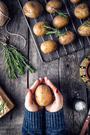Woman cooking potato with rosemary on rustic wooden background in the kitchen  の写真素材