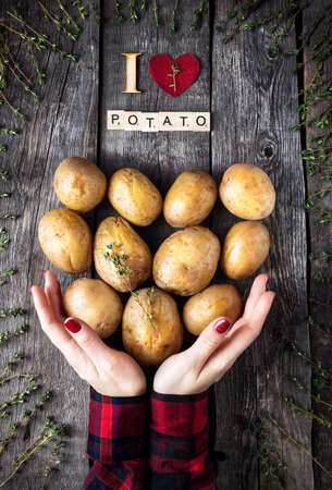 Woman holding Potato with thyme on rustic wooden background from the top viewの写真素材