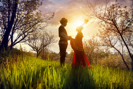 Couple in Kazakh ethnic costume in silhouette in Spring Blooming apple garden at beautiful sunsetの写真素材