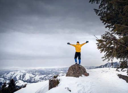 Tourist in yellow jacket with rising hands at rock in the snow mountainsの写真素材