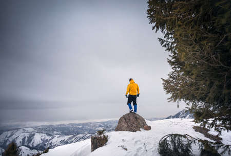Tourist in yellow jacket with standing at the top of rock in the snowy mountainsの写真素材