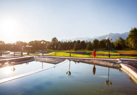Woman in orange dress near fountain at sunrise in the famous park of Almaty, Kazakhstanの写真素材