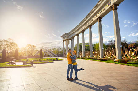 Happy couple in blue and yellow cloths hugging near column and bridge in famous park in Almaty, Kazakhstanの写真素材
