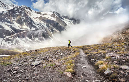 Hiker in green shirt with backpack walking in the snowy mountains at foggy sky backgroundの写真素材