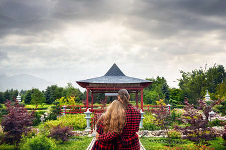 Young Couple in red checked shirts hugging and looking to the Japanese Pagoda garden at overcast skyのeditorial素材