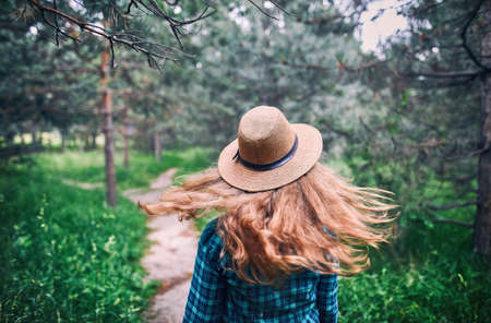 Young woman in brown hat and green checked shirt with long hair flow in the wind under pine tree in the forest の写真素材
