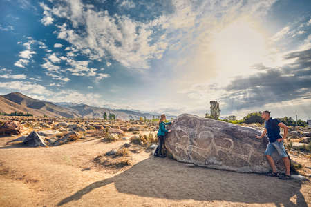 Couple in checkered shirt in the open air museum near stone with ancient petroglyph of goats at Kyrgyzstanの写真素材