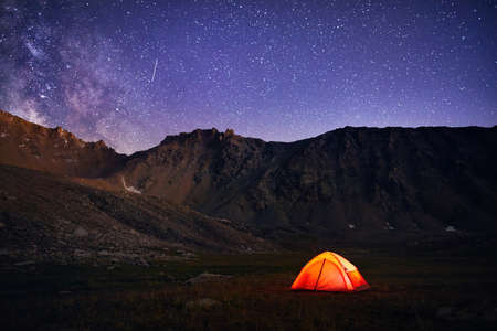 Orange tent glows under night sky full of stars and Milky way in the mountains in Kazakhstanの写真素材