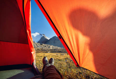 Hiker legs from orange tent with view to beautiful snowy summit