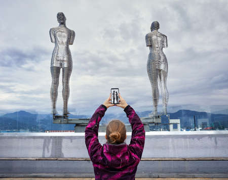 Tourist Woman tacking picture of statues Ali and Nino with smartphone in Batumi, Georgiaのeditorial素材