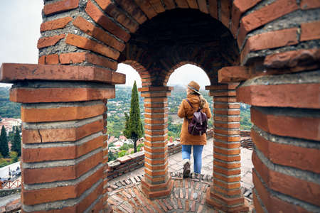 Tourist woman in hat and backpack walking in the church at autumn foggy time in Signagi, Georgia