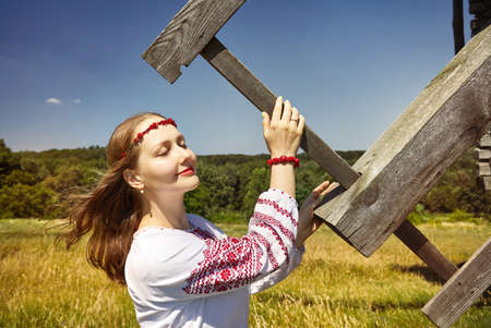 Portrait of beautiful Ukrainian girl holding blade of wooden wind mill in white ethnic shirt at architecture museum in Pirogovo. Kiev, Ukraineのeditorial素材