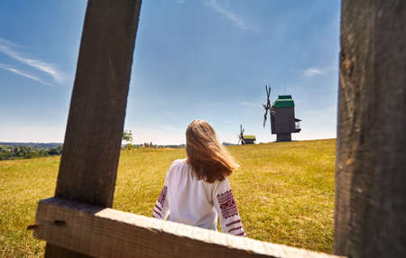 Beautiful Ukrainian girl walking near old wooden wind mills in white ethnic shirt at national architecture museum in Pirogovo. Kiev, Ukraineのeditorial素材
