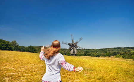Beautiful Ukrainian girl running to wooden wind mill in white ethnic shirt at national architecture museum in Pirogovo. Kiev, Ukraineの写真素材