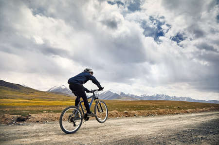 Man on mountain bike rides on the road in the high mountains against blue sky background.の写真素材