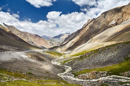 Road and white water river in the mountain valley at blue cloudy sky in Kyrgyzstanの写真素材