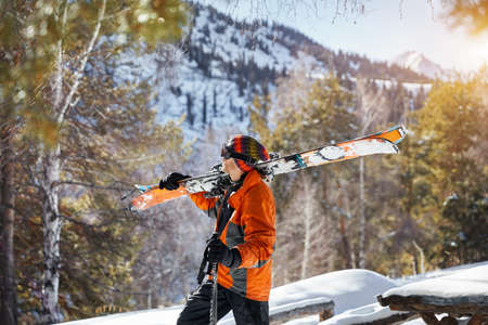 Man in orange jacket holding ski and looking at snow mountain at sunny dayの写真素材