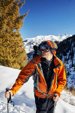 Portrait of skier in orange jacket and mask at snow mountain  at sunny day