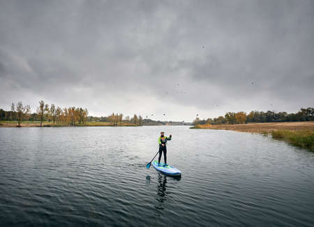 Man training on paddleboard in the lake against overcast sky