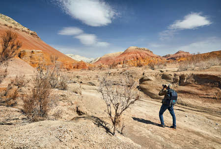 Tourist with backpack and camera taking a picture at the dusty canyon on surreal red mountains...
