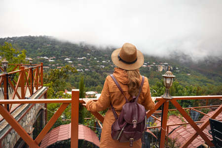 Tourist woman in hat and backpack is looking at foggy hills in Signagi, Georgia