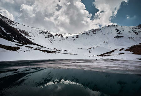 Landscape of snow mountain valley and lake with ice and reflection against cloudy sky in Kazakhstan