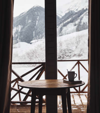 Coffee on the table with beautiful Mountain View in winter wooden cottageの写真素材