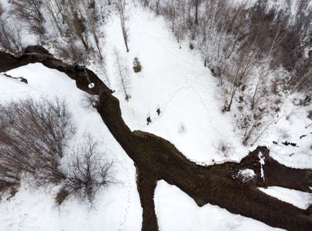 Couple of tourist is hiking in the mountain valley with river and snow at winter time in Almaty, Kazakhstan. Aerial top view, drone shot.の写真素材