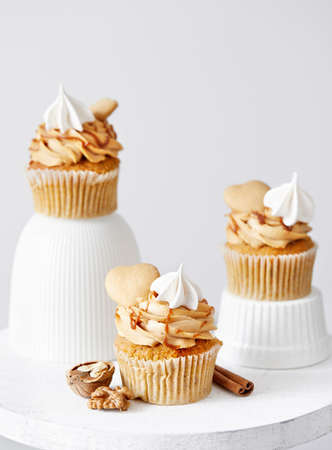 Carrot cupcakes with caramel, walnuts and spices decorated with heart shaped biscuit, meringue and salty caramel on white background. Free space for your text  の写真素材