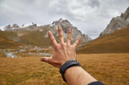 Palm of traveler man is touching beautiful scenery of the mountain valley at dramatic cloudy skyの写真素材