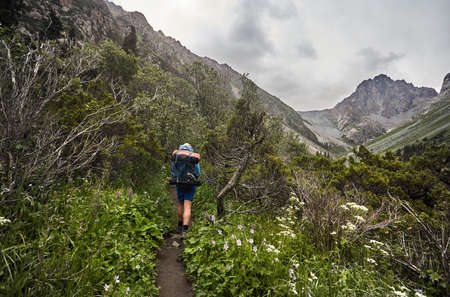 Tourist with big backpack is on the forest trail in the mountain valley of Karakol national park, Kyrgyzstanの写真素材