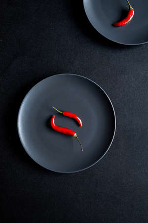 Minimalist composition of two red chili peppers in black ceramic plate at black tableの写真素材