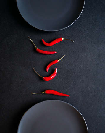 Minimalist composition of red chili peppers between two ceramic plates at black tableの写真素材