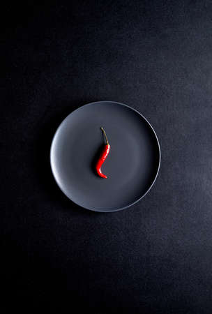 Minimalist composition of red chili pepper in black ceramic plate at black tableの写真素材