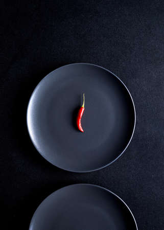Minimalist composition of red chili pepper in black ceramic plate at black tableの写真素材
