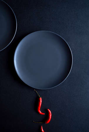 Minimalist composition of red chili peppers and two ceramic plates at black backgroundの写真素材