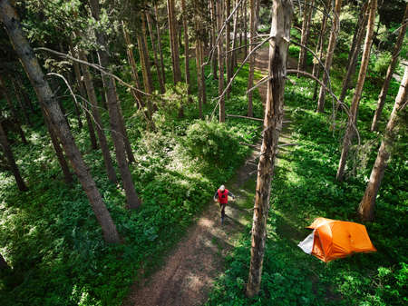 Aerial view of man walking near orange tent at forest in the mountains. Photo taken with Droneの写真素材