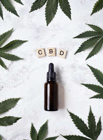 CBD oil in bottle around cannabis leaves and near wooden letters CBN on white background flat lay. の写真素材