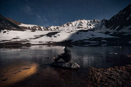 Man with his head light is looking at the lake at starry night the mountainsの写真素材