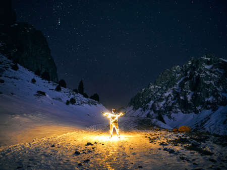 Man with Glowing orange garland in at winter mountains at dark night skyの写真素材