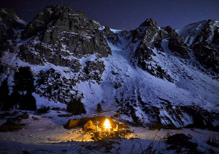 Man with Glowing orange garland in the wooden house at winter mountains at dark night skyの写真素材