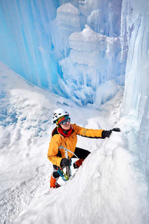 Woman climber in orange jacket with ice axe near frozen waterfall in the mountains in Almaty,...