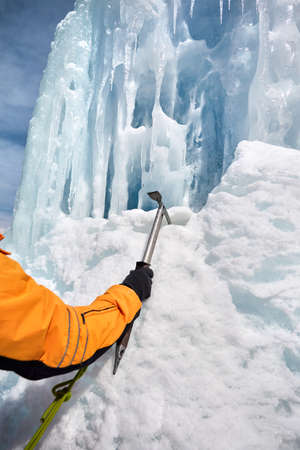 Woman climber in orange jacket with ice axe near frozen waterfall in the mountains in Almaty, Kazakhstanの写真素材