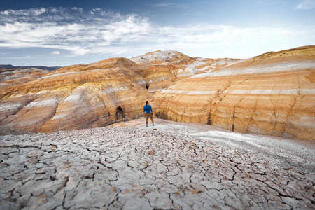 Hiker in blue shirt at drought cracked earth red striped desert mountains in Kazakhstanの写真素材