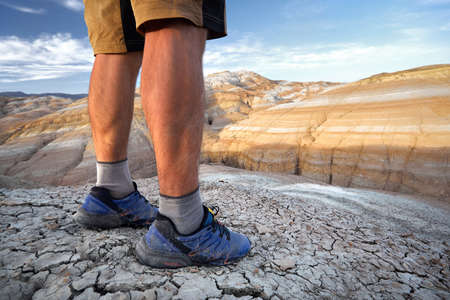 Close up of muscle legs of young runner in sport blue hoes at drought cracked earth red desert...